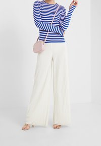 Randig blå och rosa långärmad topp, vita ribbade vida byxor, ljusrosa axelväska och nakna remsandaler.