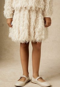 Robe fuzzy couleur crème avec des franges texturées et des sequins ; assortie à des chaussures Mary Jane beige clair avec une sangle et un petit talon.