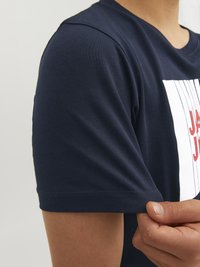 Námořnická modrá bavlněná tričko s krátkým rukávem, s bílým a červeným grafickým designem na přední straně a žebrovaným výstřihem.