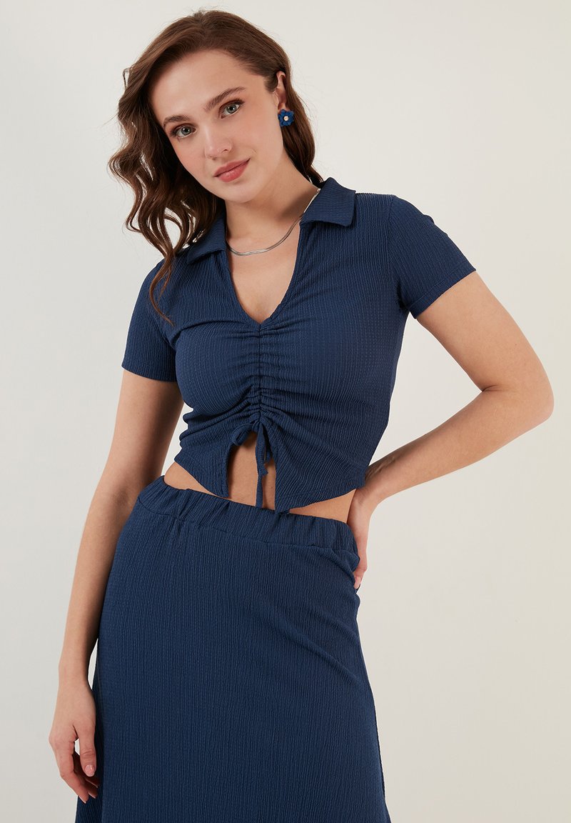 Marineblauw geribbelde crop top met korte mouwen, V-hals, geplooide details en uitsnijding in de taille, gecombineerd met een bijpassende rok.