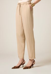 Pantalons beige, légers, à coupe ample avec une taille à cordon et des poches latérales, associés à des escarpins à talons aiguilles en imprimé léopard.