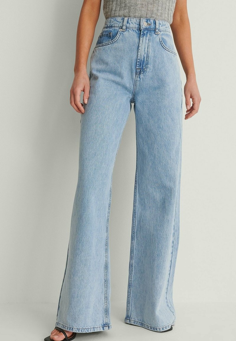 Jean large en denim bleu clair avec taille haute, poches avant et ourlet brut. Présente une texture lisse et des détails de couture visibles.