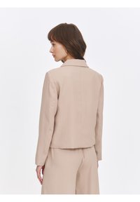 Light beige tailored jacket with a notched collar, fitted design, and smooth texture. Featured back seam detailing and long sleeves.