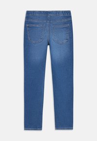 Zadný pohľad na modré denimové džínsy s dvoma zadnými vreckami a elastickým pásom, zobrazené na bielom pozadí.