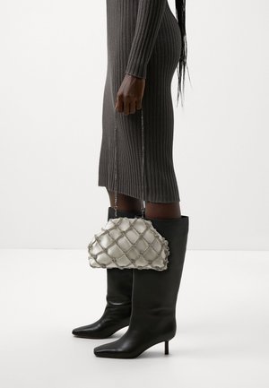 Person wearing a ribbed gray midi dress and black knee-high heeled boots, holding a white quilted handbag with netted chain detail.