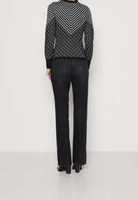 Zwarte trui met geometrische patronen en strepen op de rug, gecombineerd met donkerdenim flare jeans en zwarte haklaarzen.