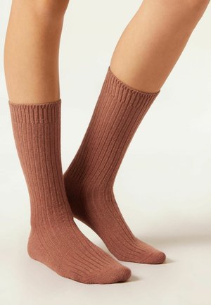 Chaussettes en tricot marron à nervures avec une texture douce, longueur mi-mollet, et bout renforcé. Design simple sans motifs ni accents supplémentaires.