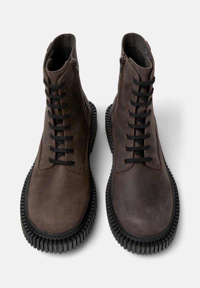 Bottines en cuir marron avec une finition lisse, présentant un bout rond, des lacets noirs et des semelles en caoutchouc texturé. Fermeture éclair sur le côté.
