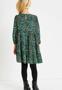 Zelené, růžové a černě vzorované šaty s dlouhými rukávy a rozšířenou sukní, s detaily ve tvaru klíčové dírky na zadní straně a doplněné černými legínami.