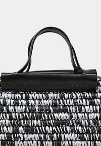 Sac en paille tressée noir et blanc avec une finition texturée, présentant un accent en cuir noir en haut et une courte poignée pour le transport.