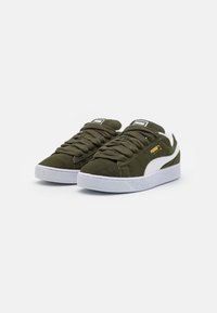 Olivegrønne ruskindsneakers med hvide gummisåler, der har tykke snørebånd og et lille guldlogo på siden. Klassisk lavtop-design.