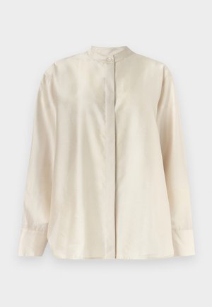 Μπλούζα κρεμ με μακριά μανίκια, όρθιο γιακά, κρυφό κουμπωτό πατιλέτα και ένα μόνο ορατό επάνω κουμπί.