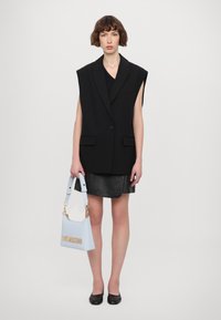 Črn oversized brezrokavnik, bluzica s V-izrezom, usnjena krila, svetlo modra torbica z napisom "LOVE MOSCHINO" v zlati barvi in črne balerinke.
