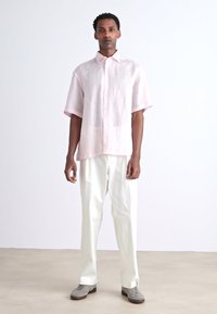 Lichtroze overhemd met korte mouwen en knopenlijst, gecombineerd met witte wijde broek en grijze schoenen. Eenvoudig ontwerp en relaxte pasvorm.