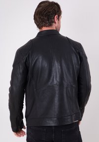 Black leather motorcycle jacket with quilted shoulder accents, fitted design, and side zipper details. Smooth texture, minimalist style.