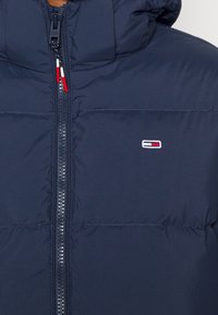 Chaqueta acolchada de color azul marino con cremallera frontal y pequeño logo rectangular en rojo, blanco y azul marino en el pecho.