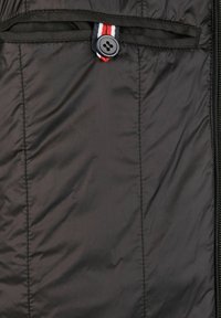 Chaqueta negra acolchada con cremallera frontal, un botón en lazo con acento de franjas roja, blanca y azul, y textura de nailon suave.