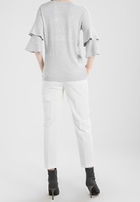Šedý pletený top s rozšířenými rukávy, zkombinovaný s bílými slim-fit kalhotami a černými vysokými kozačkami. Jednoduchý, čistý design bez vzorů.