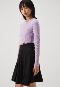 Lilac ribbed cropped top paired with a black flared skirt. The top features long sleeves and a seam detail, while the skirt has pleats.