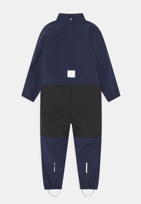 Granatowy wodoodporny kombinezon z czarną dolną częścią, z wysokim kołnierzem, elastycznymi mankietami, odblaskowymi elementami i kwadratową naszywką z logo.