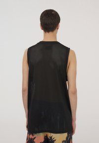 Canotta in rete nera con scollo rotondo, dotata di ampissimi fori per le braccia e design ampio sulla schiena, abbinata a pantaloni corti con un motivo colorato.