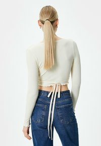 Ribbede, cropped langærmede top i lys beige med en bagbundet detalje, parret med mørkeblå jeans med klassiske lommer og en afslappet pasform.