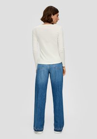 Witte lange mouwen top gecombineerd met een wijde blauwe jeans met een klassieke vijf-pocket ontwerp en subtiele stiksels aan de zoom.