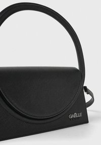 Borsa nera realizzata in materiale strutturato, con una patta arrotondata, un manico singolo e una tracolla removibile. Brandizzazione evidente sul lato.