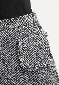 Tissu à motif chevrons en noir et blanc avec une finition texturée, présentant un détail de poche effilochée sur le côté.