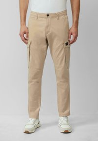 Beżowe spodnie cargo o slim fit, wyposażone w boczne kieszenie, szlufki na pasek oraz zapięcie na guzik. Wykonane z lekkiego materiału dla komfortu.