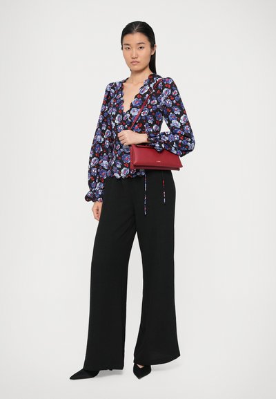 Blusa floreale blu navy con fiori rosa e blu, orlo volant, abbinata a pantaloni larghi neri e una borsa a tracolla rossa.