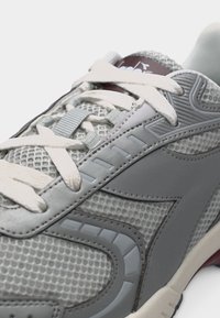 Κοντινή λήψη ενός γκρι και λευκού αθλητικού παπουτσιού με λεπτομέρειες από δίχτυ, λευκά κορδόνια και υφή δερμάτινων επιφανειών.