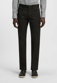Black trousers with a straight cut, made from a smooth fabric. Features front pockets, a button closure, and paired with black shoes.