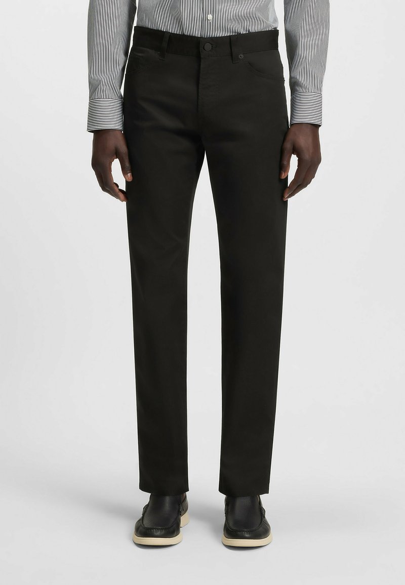 Black trousers with a straight cut, made from a smooth fabric. Features front pockets, a button closure, and paired with black shoes.