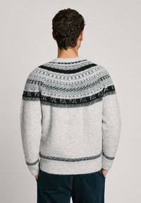 Pull gris clair avec un empiècement texturé et à motifs en noir et gris foncé. Présente des poignets et un ourlet côtelés, fabriqué en tissu doux.