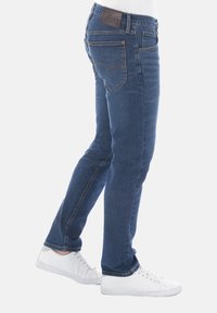 Vaqueros de mezclilla azul con un corte Slim, que presentan una etiqueta de cuero en la cinturilla, un clásico diseño de cinco bolsillos y detalles de costura sutiles.