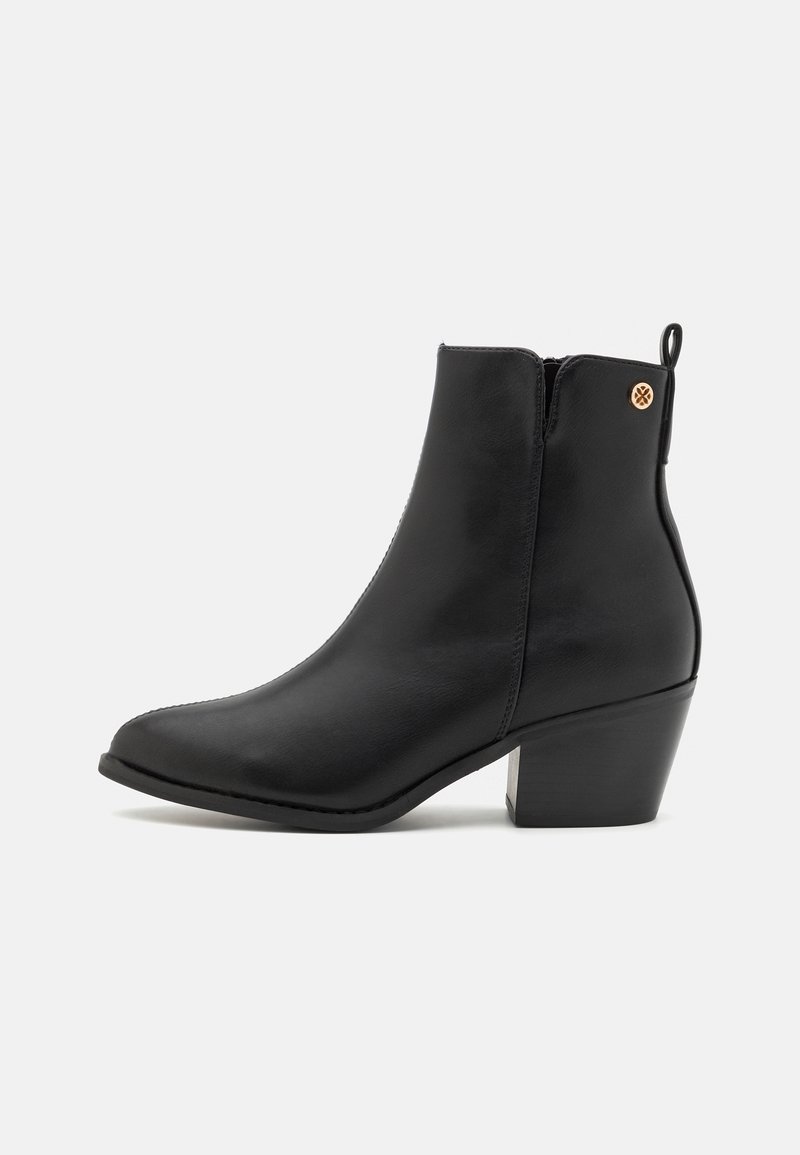 Bottine en cuir noir avec bout pointu, talon bloc de hauteur moyenne, fermeture éclair latérale et accent métallique décoratif à l'arrière.