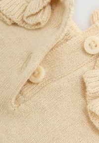 Cream-colored knitted fabric with two cream buttons and ruffled knitted edging.