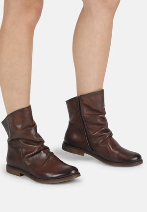 Botas de cuero marrón hasta el tobillo con un diseño holgado, cierre lateral con cremallera y suela plana. El material tiene una textura suave con detalles de costura sutiles.
