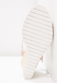 Sandale à talon compensé beige avec une semelle intermédiaire en espadrille texturée, dotée d'une semelle extérieure en caoutchouc blanc avec des rainures parallèles, et d'un design de bride minimaliste.