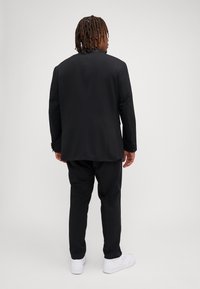 Black suit featuring a tailored blazer and matching trousers. Smooth fabric with a sleek design, paired with white sneakers for a modern touch.