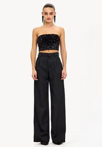 Top corto sin mangas negro con lentejuelas, combinado con pantalones negros de pierna ancha y cintura alta. Textura suave con una silueta ajustada.