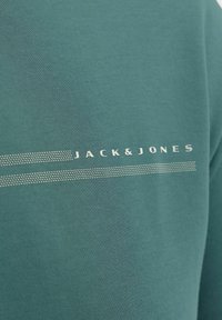 Φούτερ από μείγμα βαμβακιού σε τιρκουάζ με στρογγυλή λαιμόκοψη. Διαθέτει ασημί λογότυπο "JACK&JONES" και διακοσμητικές διακεκομμένες γραμμές. Λεία υφή.
