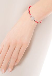 Czerwony sznurkowy bransoletka z srebrnym zawieszką w kształcie płatka śniegu, ozdobiona małymi srebrnymi koralikami i okrągłą zawieszką.
