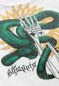 Bela majica s printom zeleni kač, ki se prepleta s kostnim dlanjo in vzorci strele; vključuje črn napis "All Saints".