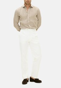 Camicia a righe beige con bottoni, pantaloni bianchi e scarpe in suede marroni. La camicia presenta un colletto classico e un tessuto testurizzato.