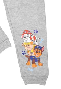 Pantaloni grigi in felpa con un motivo di cuccioli di cartone animato, uno dei quali indossa un casco da pompiere, uno in uniforme di polizia, e dettagli a forma di impronta di zampa.