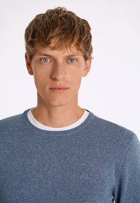 Maglione blu girocollo con scollo a coste, realizzato in materiale morbido, caratterizzato da un delicato motivo testurizzato e un logo ricamato sul petto.