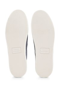 Två vita skosulor med texturerat grepp och "Tommy Hilfiger"-logotyp präglad nära hälen, sedda från botten.