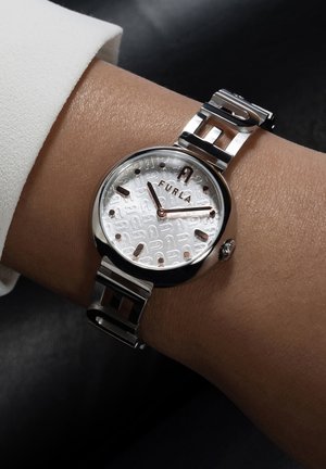 Montre en acier inoxydable argenté avec un cadran rond, un cadran texturé blanc et des accents en or rose. Elle possède un bracelet à maillons et un détail de logo proéminent.